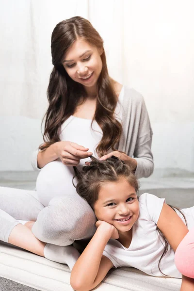 Gravid kvinna med dotter sitter på matta — Stockfoto