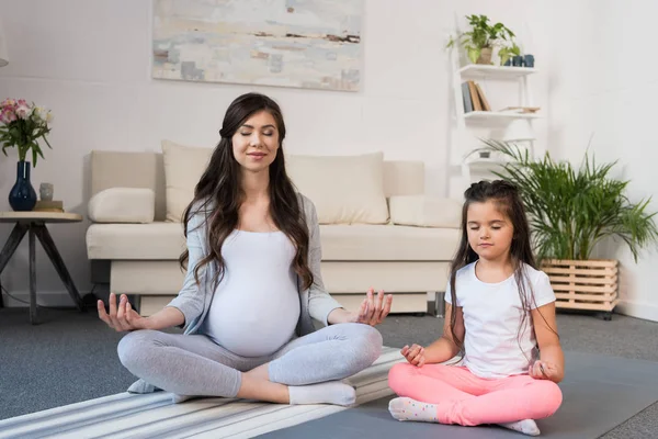 Pregnant woman with daughter in lotus pose — Stock Photo, Image