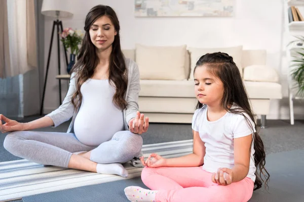 Pregnant woman with daughter in lotus pose — Stock Photo, Image