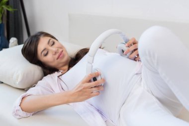 Pregnant woman holding headphones   clipart