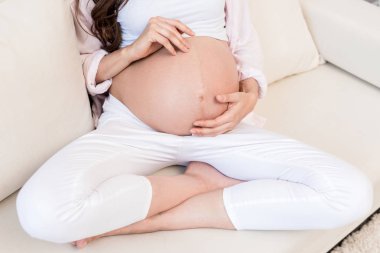 Pregnant woman touching her belly on couch clipart