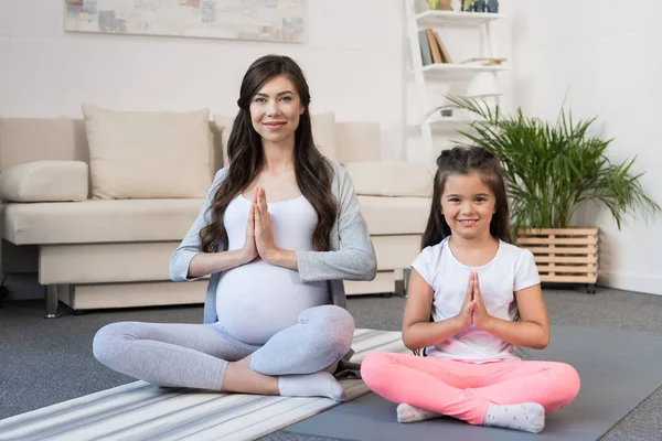 Pregnant woman with daughter in lotus pose — Free Stock Photo