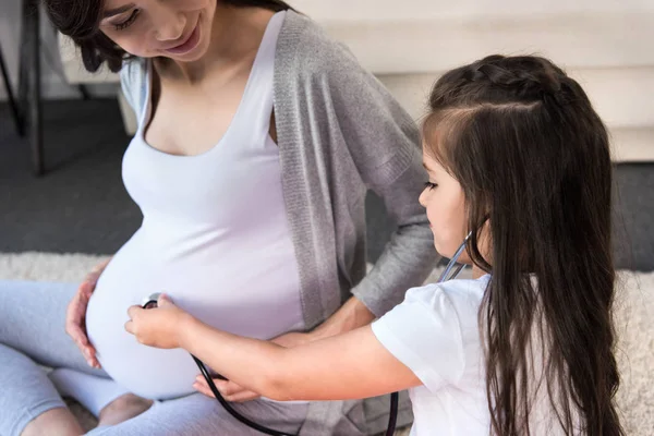 Girl listening to pregnant belly through stethoscope — Stock Photo, Image