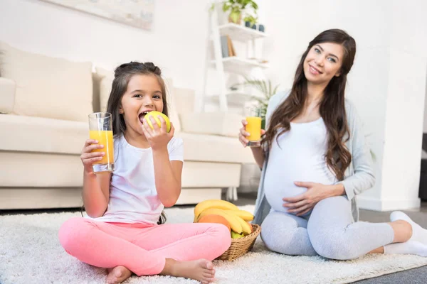 Pregnant woman and daughter with glasses of juice — Stock Photo, Image