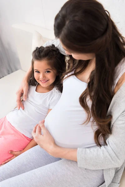 Femme enceinte étreignant fille sur le canapé — Photo