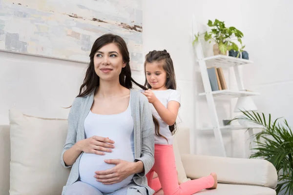 Little girl braiding hair of pregnant mother — Stock Photo, Image