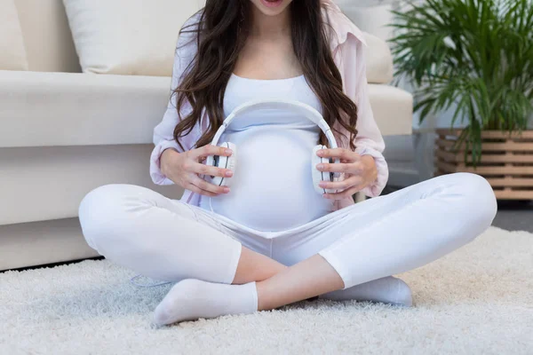Беременная женщина держит наушники над животом — стоковое фото