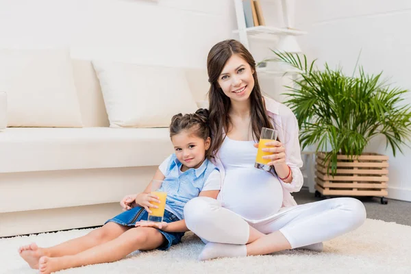 Mujer embarazada e hija con vasos de jugo — Foto de Stock