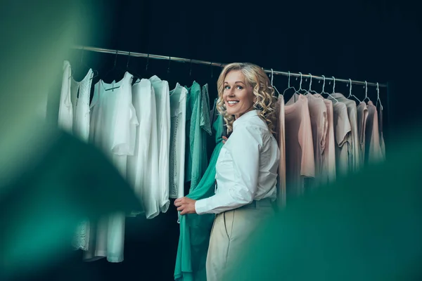 Улыбающаяся женщина выбирает одежду в магазине — стоковое фото