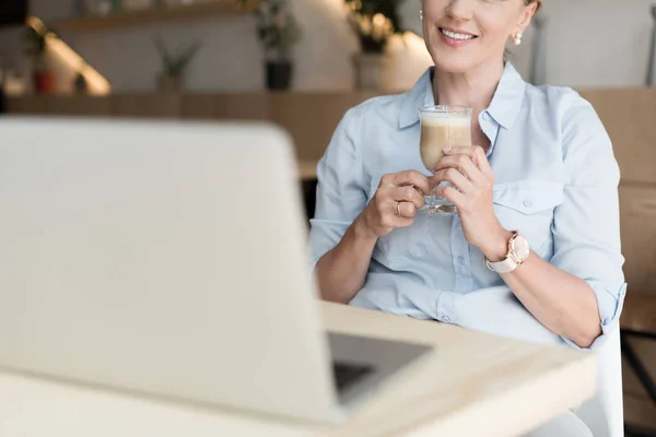 Woman drinking coffee and using laptop — Free Stock Photo