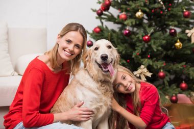 Anne ve kızı köpeği kucaklıyor.