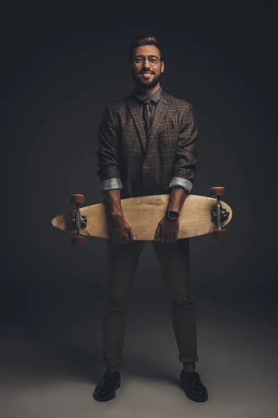Человек в костюме держит скейтборд — стоковое фото