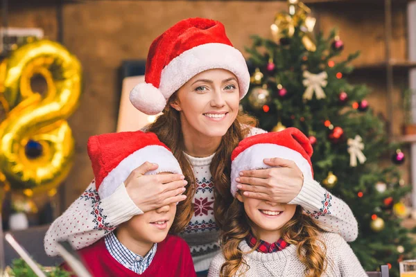 Mãe abraçando com crianças em chapéus de santa — Fotografia de Stock