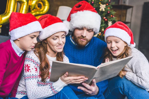 Kitap okuma Noel Baba şapkaları ailede — Stok fotoğraf