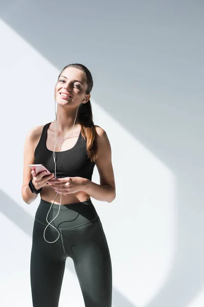 Sportswoman in earphones using smartphone — Stock Photo, Image