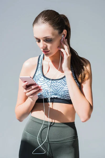 Sportswoman in earphones using smartphone — Free Stock Photo