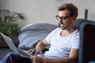 Dizüstü bilgisayar kullanarak koltuk gülümseyen adam