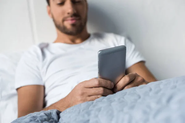 Muž používající smartphone v posteli — Stock fotografie