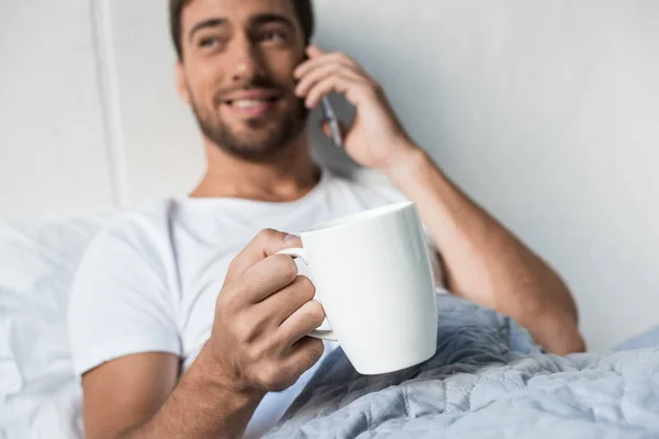 Ο άνθρωπος στο τηλέφωνο που πίνει καφέ στο κρεβάτι — Φωτογραφία Αρχείου
