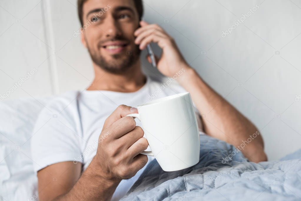 man on phone drinking coffee in bed