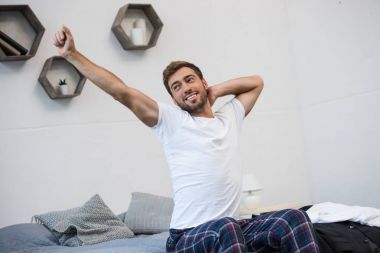 Smiling man stretching on bed clipart