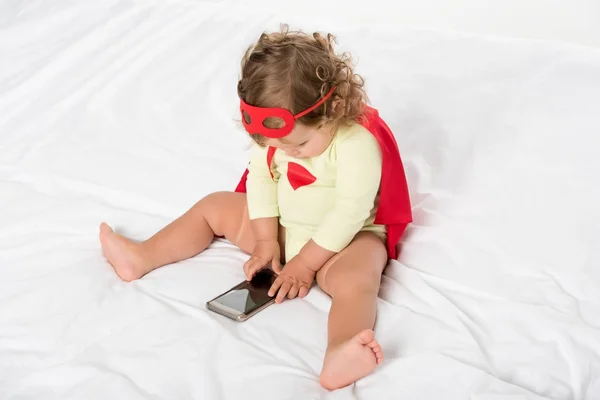 Малыш в костюме супергероя со смартфоном — стоковое фото