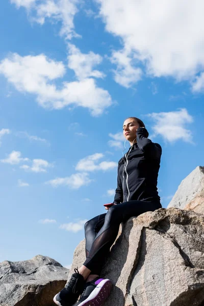 Woman sitting on rocks and listening music — Free Stock Photo