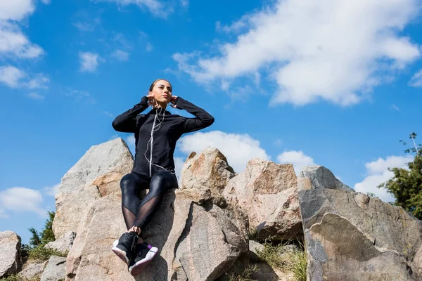 Kvinnan sitter på klipporna och lyssnar musik — Stockfoto