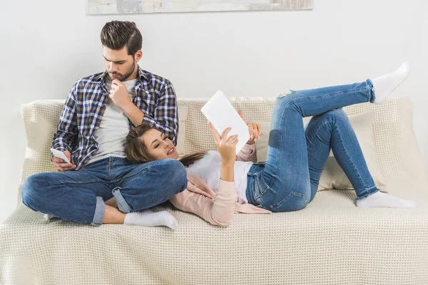 Par på soffan med enheter — Stockfoto