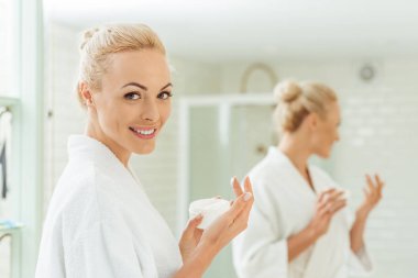 woman in bathrobe applying face cream clipart
