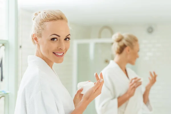 Mujer en albornoz aplicando crema facial — Foto de Stock