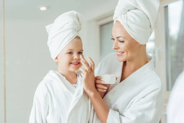 Mãe e filha aplicando creme facial — Fotografia de Stock