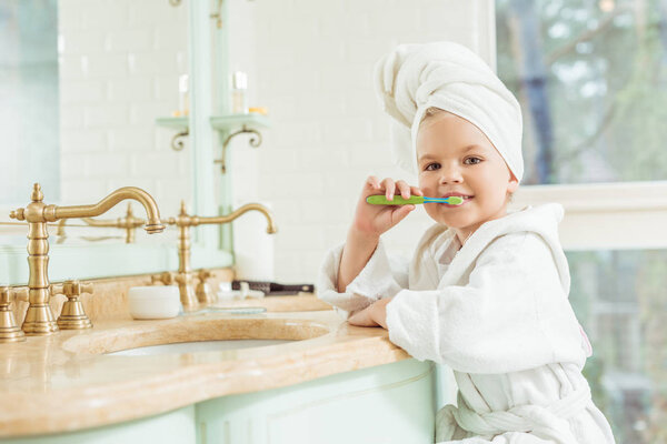 child in bathrobe brushing teeth