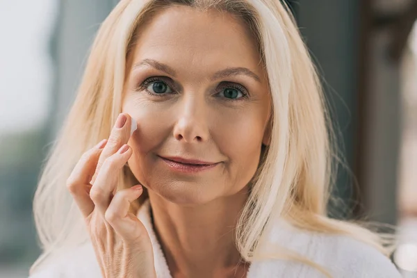 Mature woman applying cosmetic cream — Stock Photo, Image