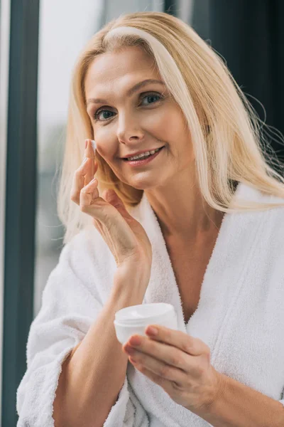 Mulher madura aplicando creme cosmético — Fotografia de Stock
