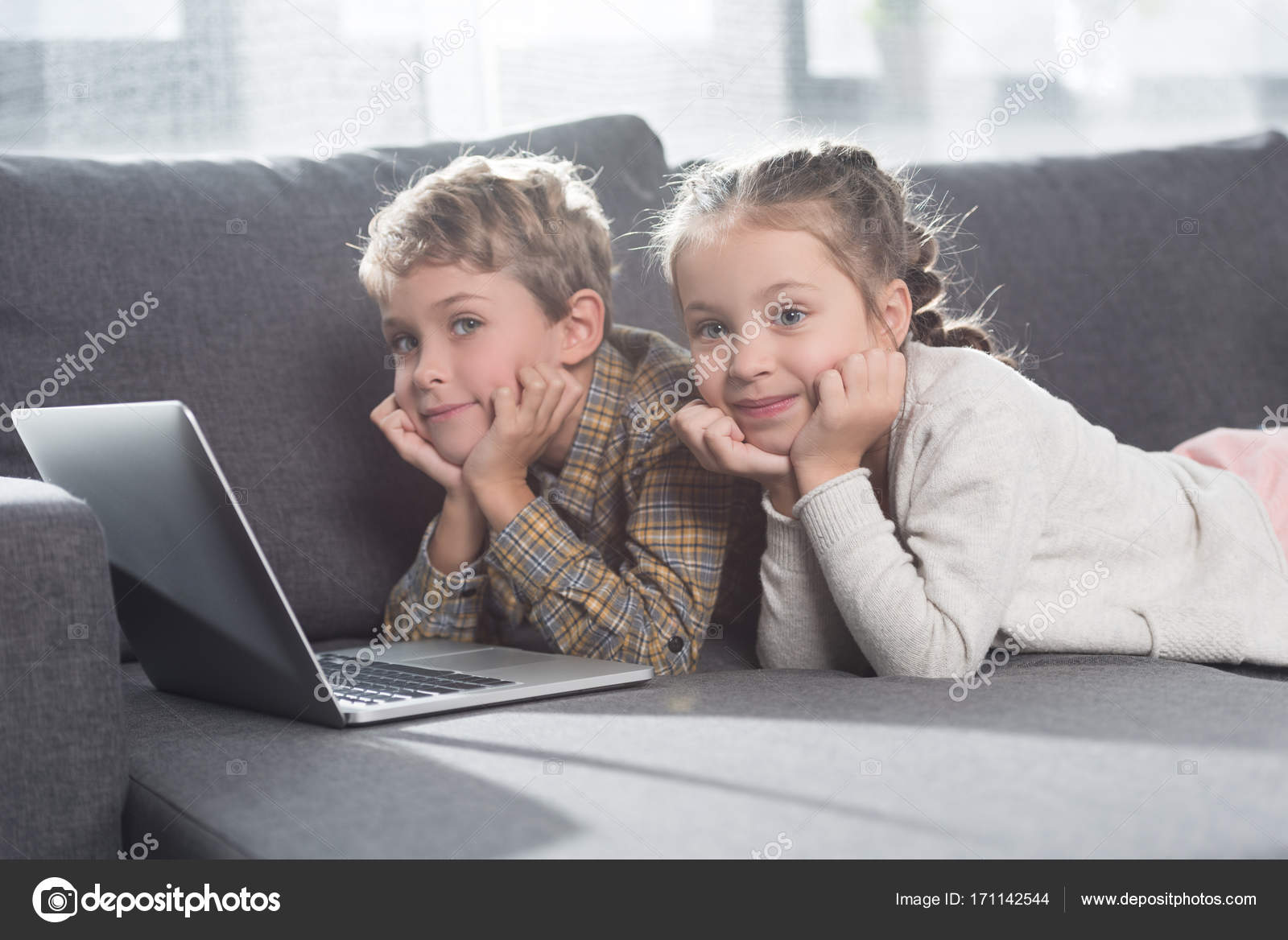 Dos niños sonrientes que usan laptop delante de una tableta. - Foto de