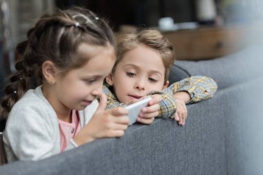 kids on couch using smartphone clipart