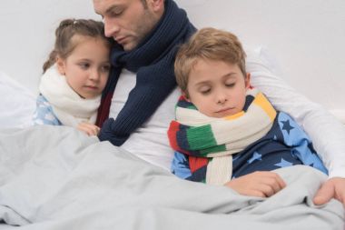 Sick father with son and daughter in bed  clipart