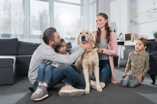 Семья сидит на полу с собакой
 