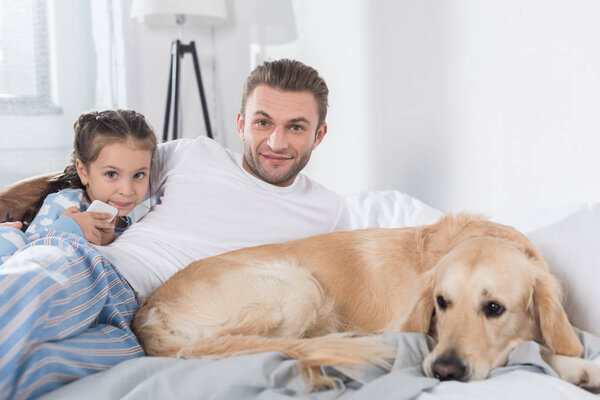 Father and daughter with dog in bed