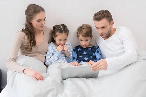 Dizüstü bilgisayar ile yatakta yalan aile — Stok fotoğraf