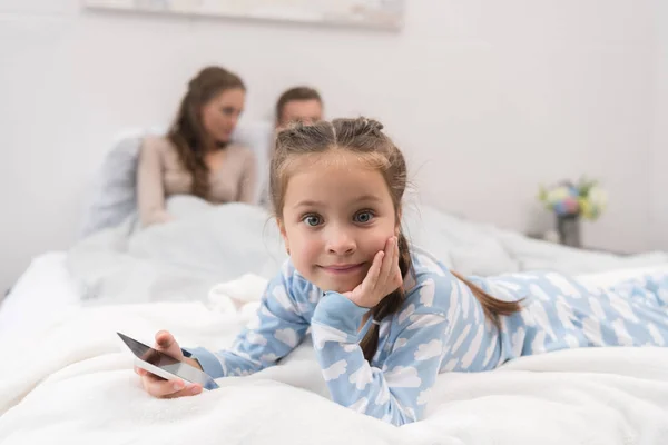 Дочь лежит на кровати со смартфоном — стоковое фото
