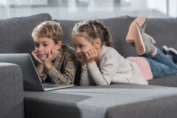 Kids lying on sofa with laptop — Stock Photo, Image