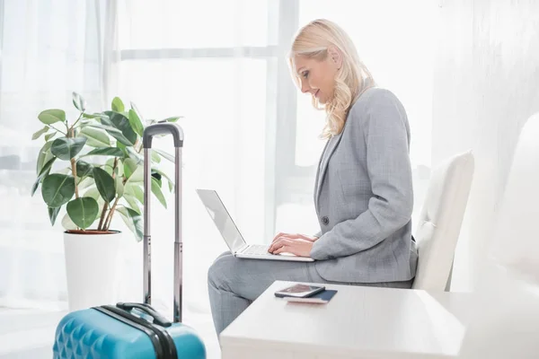 Businesswoman with luggage using laptop — Stock Photo, Image