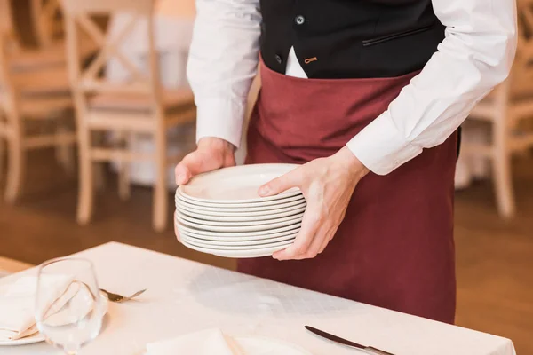 Waiter putting pile of plates on table — Stock Photo, Image