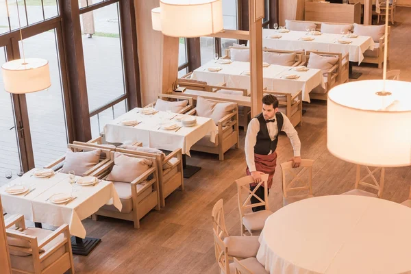 Waiter putting chairs around table — Stock Photo, Image