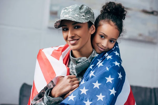 Filha e soldado envolto com bandeira americana — Fotografia de Stock