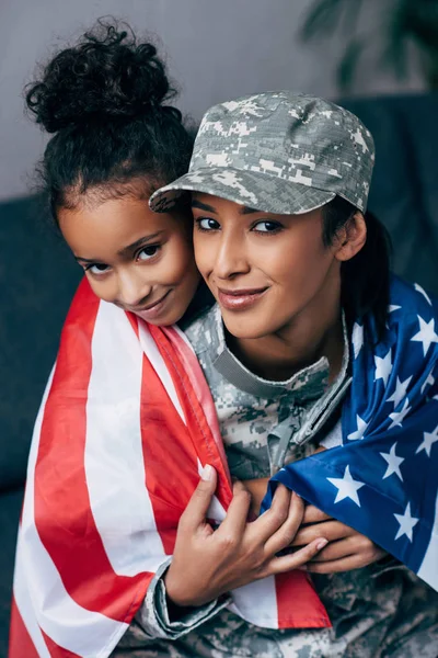 Filha e soldado envolto com bandeira americana — Fotografia de Stock