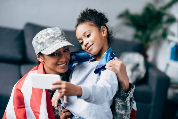 Figlia e soldato con bandiera scattare selfie — Foto Stock