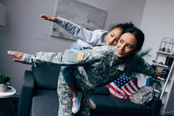 Mother in military uniform piggybacking daughter — Stock Photo, Image
